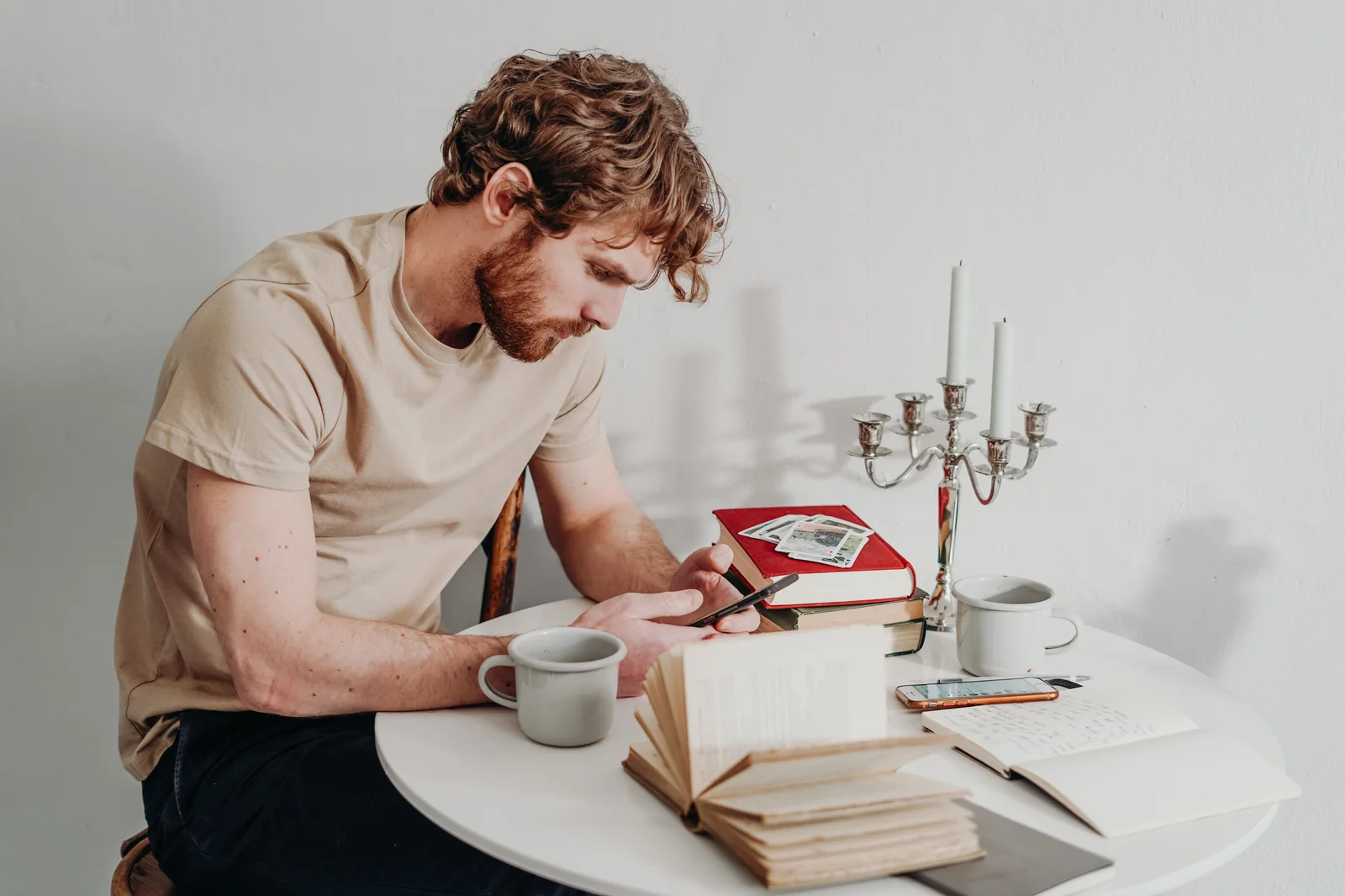 Man seated at a table reviewing content on his smartphone with books and a notebook nearby