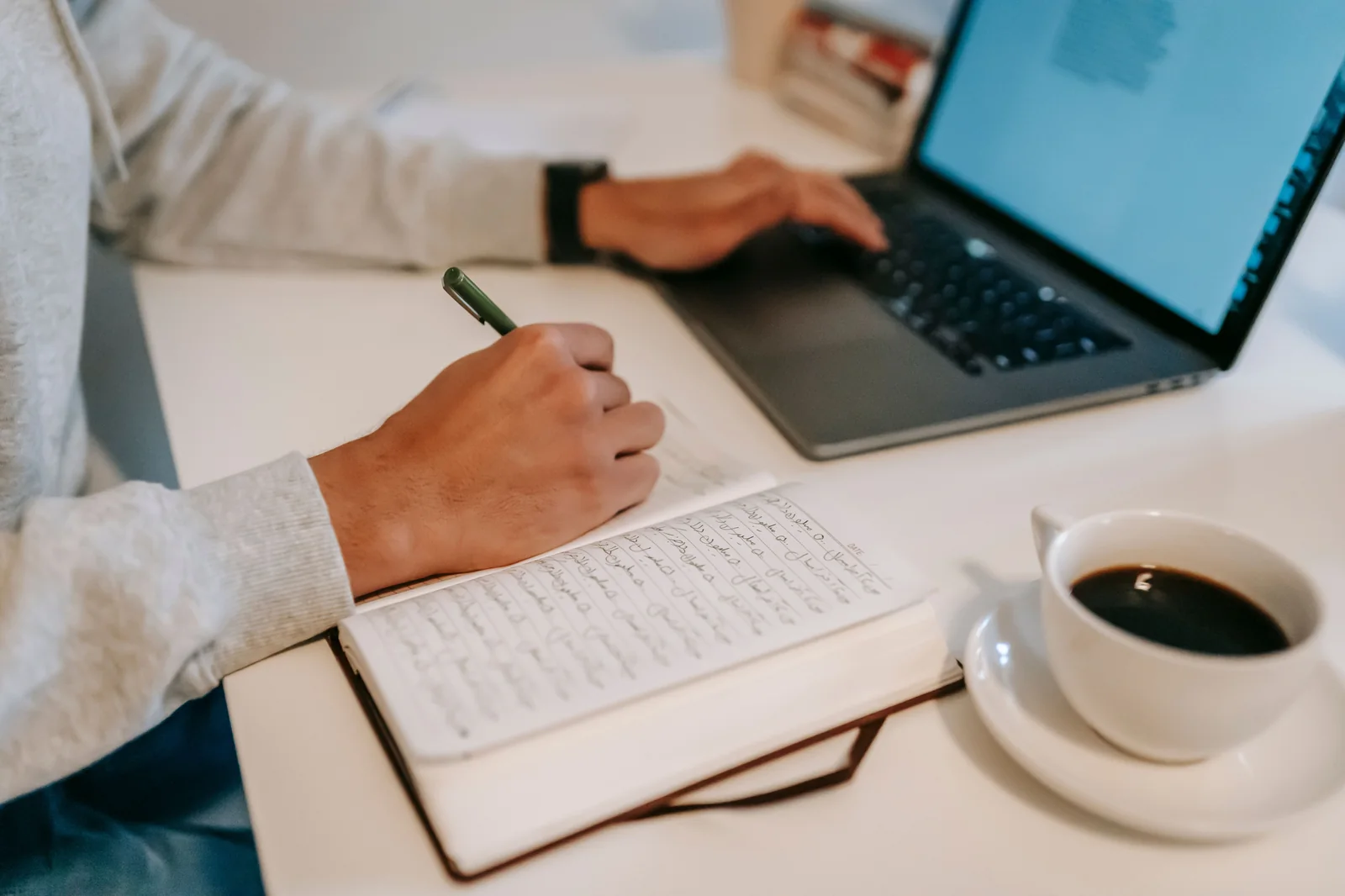 Writer taking handwritten notes in an open notebook while working on a laptop at a desk