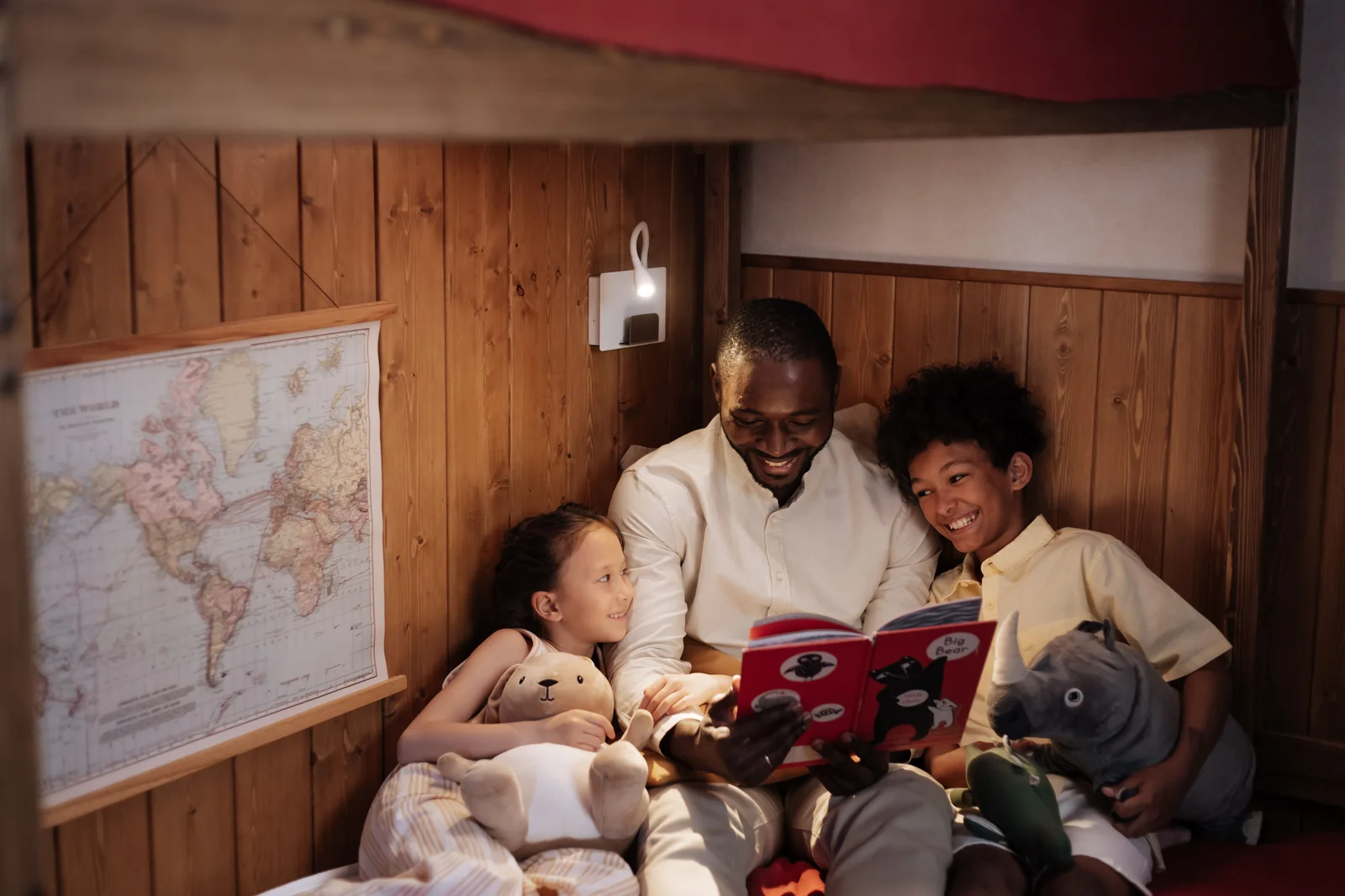 Father reading an illustrated storybook aloud to two smiling children in a cozy bunk bed at night