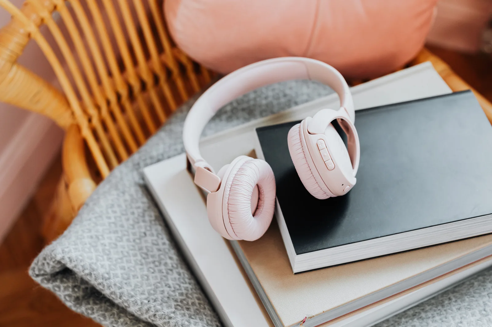 Pink wireless headphones resting on a stack of books on a chair